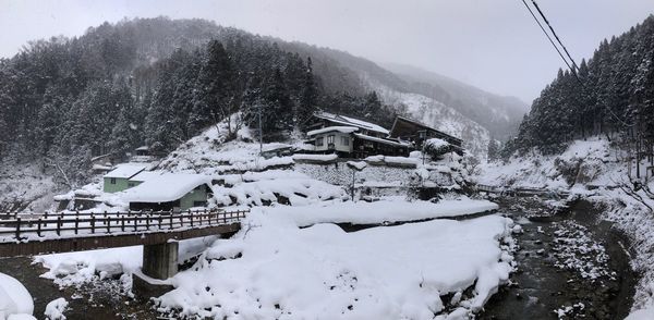 Snow covered field by trees and houses against sky