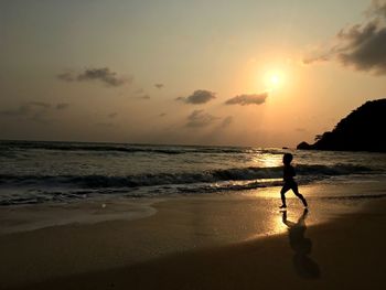 Silhouette child on beach against sky during sunset