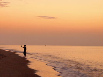 Silhouette woman on beach against sky during sunset