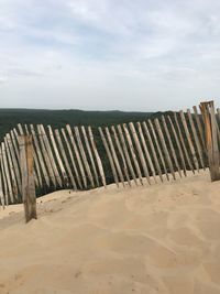 Wooden fence on beach against sky