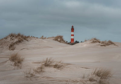 Lighthouse on snow covered landscape against sky