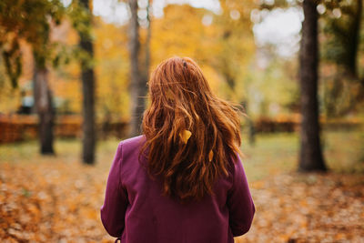 Back view faceless portrait of red-haired girl with fall leaves in hair. autumn portrait of happy