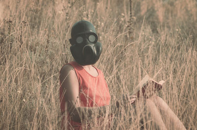 Portrait of woman wearing gas mask while holding book by plants