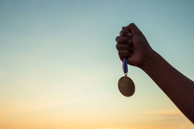 Midsection of man holding hanging against sky during sunset