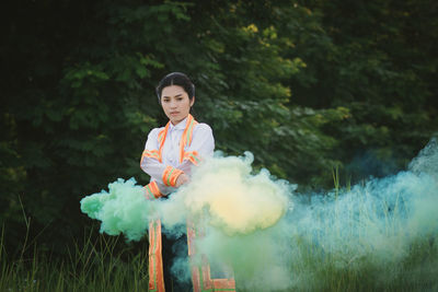 Portrait of woman holding distress flare while standing on field