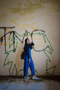 Full length of young woman standing against graffiti wall