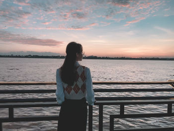 Rear view of woman standing at beach against sky during sunset