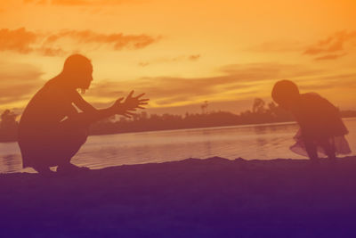 Silhouette people on beach against orange sky