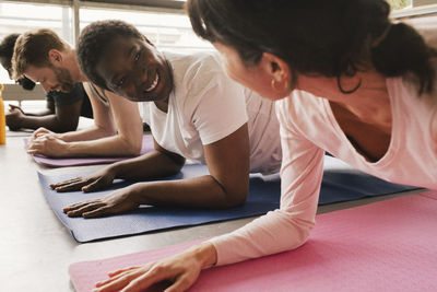 Smiling businesswoman practicing plank position with colleagues on exercise mats at office