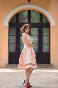 Full length portrait of woman standing against building