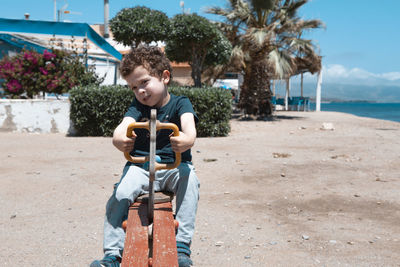  boy with curly hair riding on a seesaw on the beach  