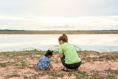 Rear view of women sitting on land against sky