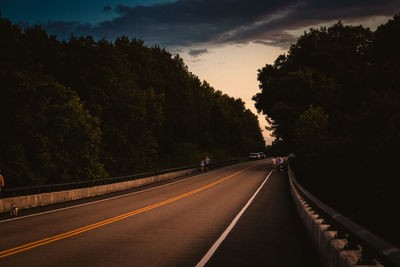 Road amidst trees against sky during sunset