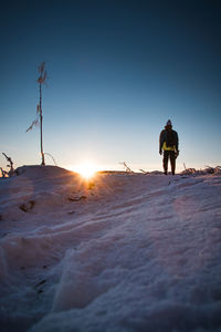 Rear view of man on snow covered land against sky during sunset