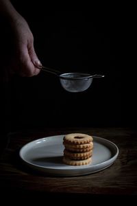 Close-up of hand holding sieve over cookies in plate on table