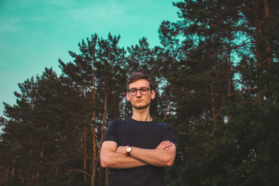 Portrait of young man standing against trees