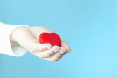 Female hand holds a red heart on a blue background.
