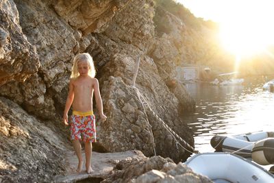 Full length of shirtless boy standing on rock at shore