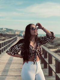 Young woman wearing sunglasses standing against sky