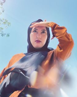 Low angle portrait of woman against blue sky