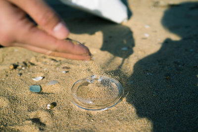 Cropped hand of person putting sand on glass container