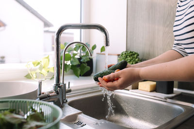 Woman washing green cucumbers for salad in kitchen in sink under running water. high quality photo