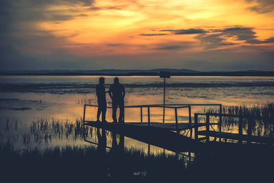 Silhouette people standing on beach against sky during sunset