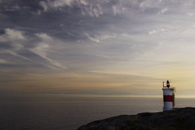 Lighthouse by sea against sky during sunset
