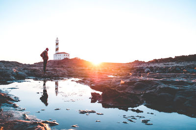 Man standing on rock against sky during sunset