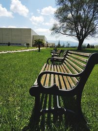 Empty park bench on field against sky