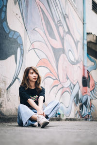 Full length of young woman sitting on wall