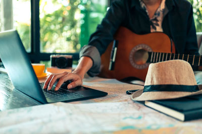 Close-up of man holding guitar while using laptop indoors