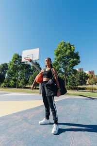 Confident sportswoman with basketball in sports court on sunny day