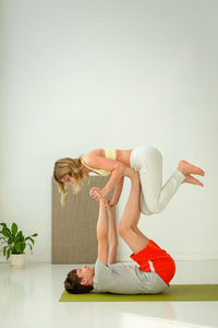 A guy in sportswear performs a yoga exercise while on a sports mat, paired with a slender woman.