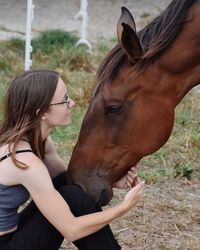 Side view of woman sitting by horse on field