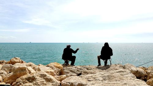 People on rocks by sea against sky