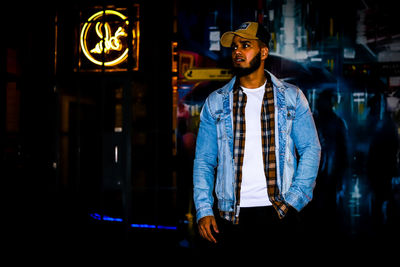 Young man standing against illuminated wall at night