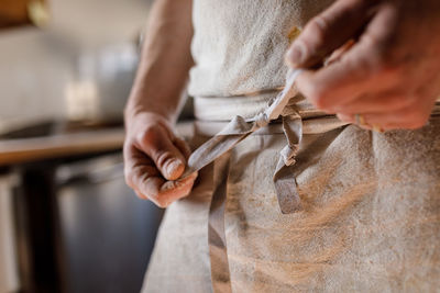 Midsection of woman tying apron in kitchen