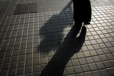 Low section of silhouette person on footpath during sunny day