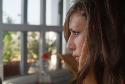 Close-up of thoughtful young woman looking through window at home