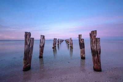 Wooden posts on beach against sky during sunset