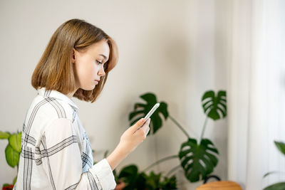 Young woman holding smartphone using mobile apps, chatting in social media at home.