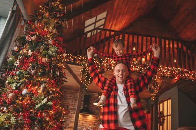 Candid authentic happy dad and son in red plaid pajamas fooling around at wood lodge xmas decorated