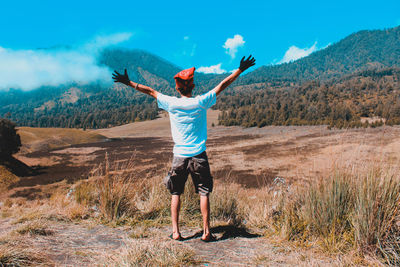 Rear view full length of man with arms outstretched standing against mountains