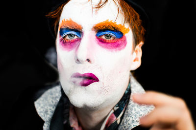 Close-up portrait of man with face paint smoking against black background