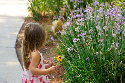 Girl holding flower while standing by plant