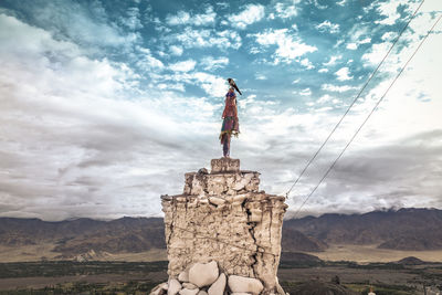 Crow sitting on the sculpture on rock against sky