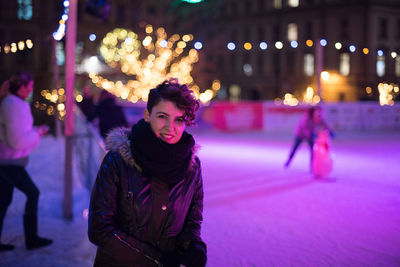 Portrait of happy woman standing by railing at night during christmas