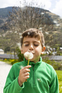 Cute boy blowing dandelion on field