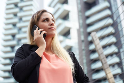 Young woman using phone while standing against buildings